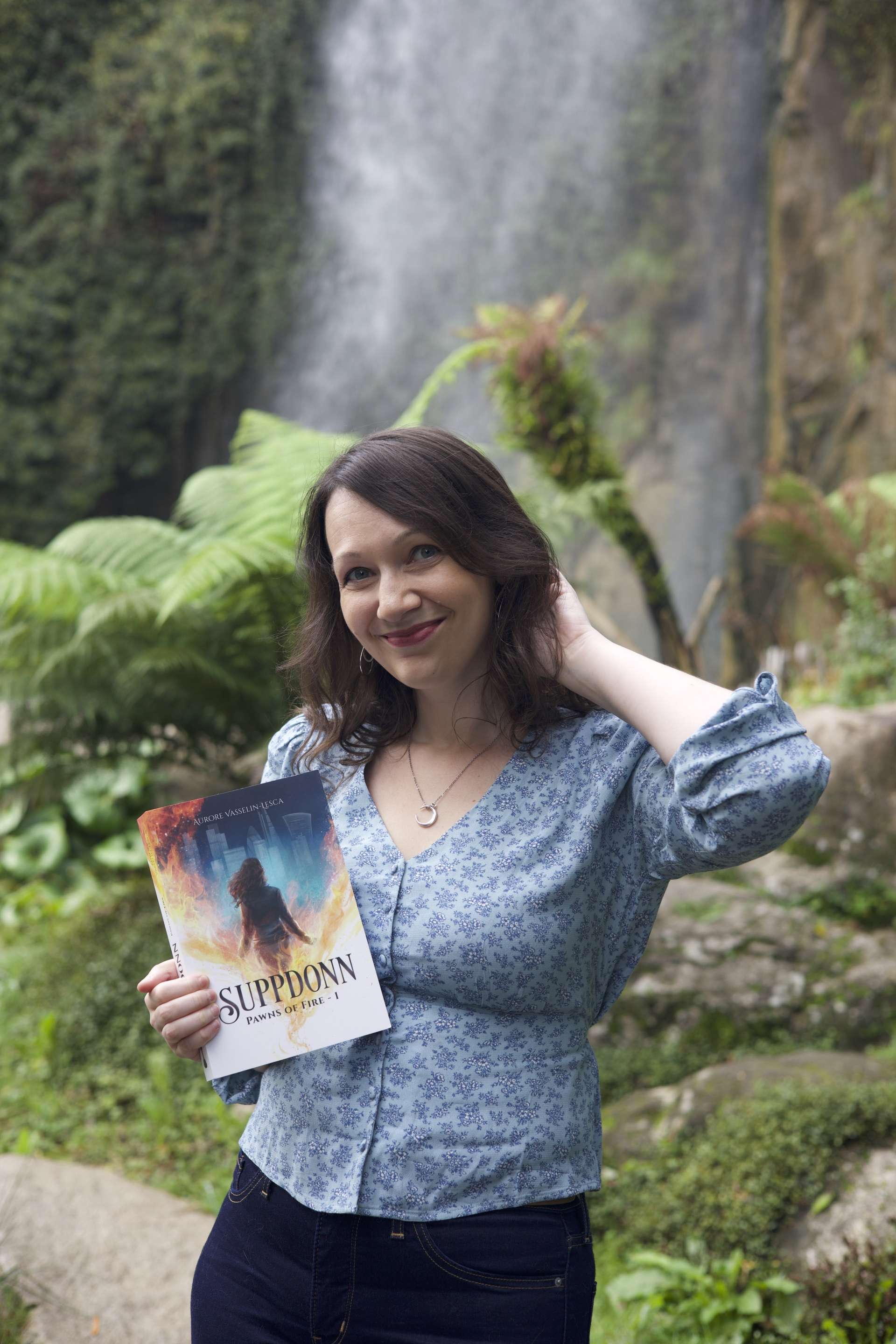 Aurore Vasselin-Lesca debout devant une cascade d'eau avec son livre Suppdoww tome 1